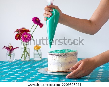 Woman spreading the icing to cover the top of the cake. Home baking, handmade. Free time on quarantine. Confectioner hands topping a cake with mint filling using a pastry bag. Selective focus.