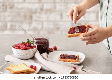 Woman spreading sweet raspberry jam on toast in kitchen - Powered by Shutterstock