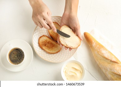 Woman spreading tasty butter onto bread over plate at white table, top view