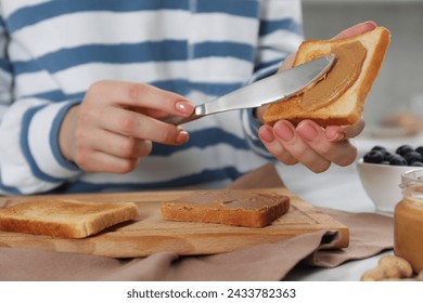 Woman spreading tasty nut butter onto toast at table, closeup - Powered by Shutterstock