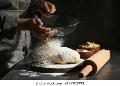 Woman sprinkling flour over dough at black table, closeup - Powered by Shutterstock