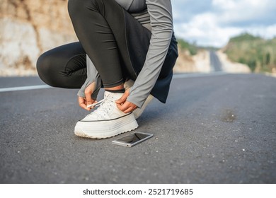 woman in squat position tying shoelace with phone beside her, cropped picture - Powered by Shutterstock