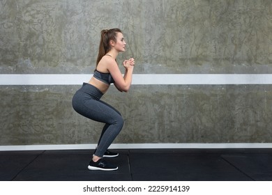 Woman squatting with her arms in front of her chest, trainer shows exercise for glutes at the gym