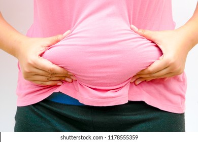 A woman squeeze her tummy.She has a beer belly or potbelly and excessive abdominal fat around the stomach and abdomen has built up to the extent that it is likely to have a negative impact on health