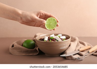 Woman squeezing fresh lime juice onto tasty lentils with cheese in bowl