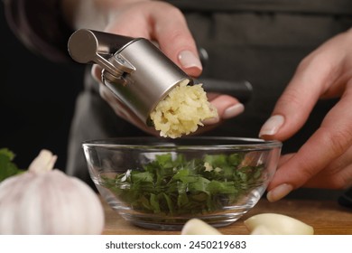 Woman squeezing garlic with press at table, closeup