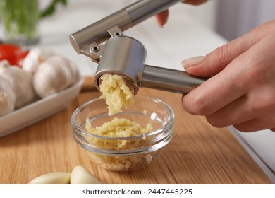 Woman squeezing garlic with press at wooden table, closeup