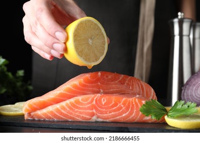 Woman Squeezing Lemon Onto Fresh Raw Salmon At Table, Closeup. Fish Delicacy