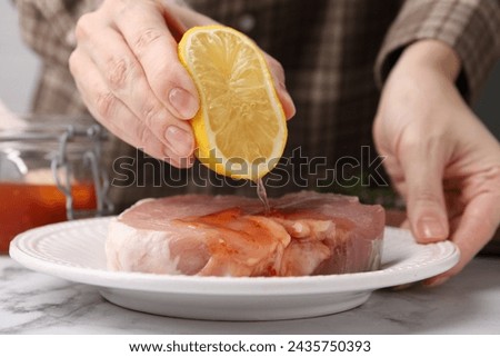 Woman squeezing lemon onto raw marinated meat at white marble table, closeup