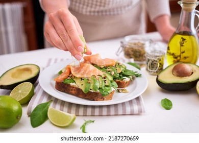 Woman Squeezing Lime Juice On Freshly Made Avocado, Salmon And Cream Cheese Toasts