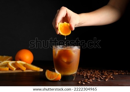 Woman squeezing orange juice into glass of refreshing drink with coffee at wooden table, closeup