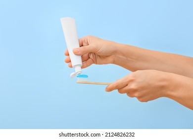 Woman Squeezing Tooth Paste Onto Brush On Blue Background