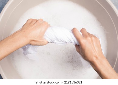 Woman squeezing wet clothes with two hands, washing white clothes, hand washing, laundry concept - Shutterstock ID 2191536321