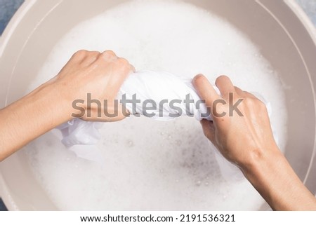 Woman squeezing wet clothes with two hands, washing white clothes, hand washing, laundry concept
