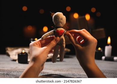 Woman stabbing voodoo doll with pin at wooden table indoors, closeup