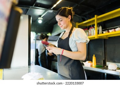 Woman stall vendor at the food truck checking the customers orders on the delivery app on the smartphone