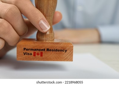 Woman stamping document at white wooden table, closeup. Permanent residency visa in Canada - Shutterstock ID 2218968055