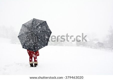 A woman stand alone in snow storm watching  falling snow in the village, Red dress woman holding black umbrella standing in snow storm, Lonely woman in the winter wonderland