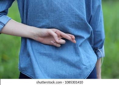 a woman stand back and do cross finger at her back of blue jean shirt on the green garden background
