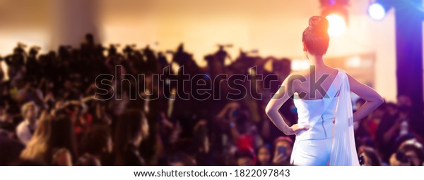 Woman stand in front\
of Media Press Television camera as Model Fashion Show or Miss\
Beauty queen pageant contest to empower people, Light to back view\
of unrecognizable woman