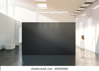 Woman stand near blank black wall mockup in modern white gallery. Girl walk near dark big stand mock up in museum with contemporary art exhibitions. Large hall interior, grey banner exposition