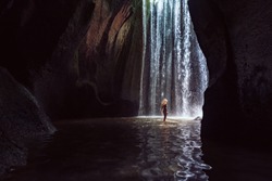 Woman Stand In Underground Cave Pool Under Falling Fresh Water Of Tukad Cepung Waterfall. Nature Day Tour, Hiking Activity Adventure And Fun At Family Tourist Camp On Summer Vacation In Bali Island
