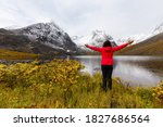 Woman standing with Arms up at Beautifil Alpine Lake surrounded by Snowy Mountains in Canadian Nature. Season change from Fall to Winter. Grizzly Lake in Tombstone Territorial Park, Yukon, Canada.