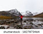 Woman standing with Arms up at Beautifil Alpine Lake surrounded by Snowy Mountains in Canadian Nature. Taken at Grizzly Lake in Tombstone Territorial Park, Yukon, Canada.
