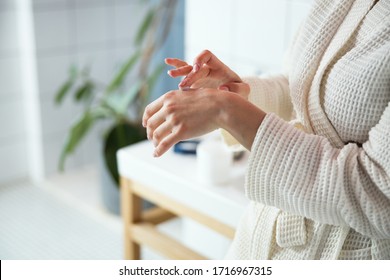 Woman is standing in bathroom and putting some cream for softening skin on her palms
