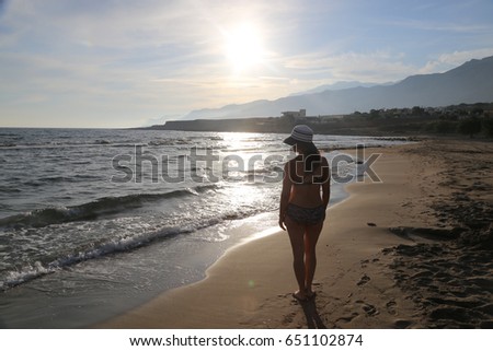 woman standing in bikini wearing a hat at a mediterranean  beach at sunset 