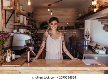 Woman Standing At The Billing Counter Of Her Cafe Posing. Smiling Restaurant Owner Standing Beside The Billing Machine.