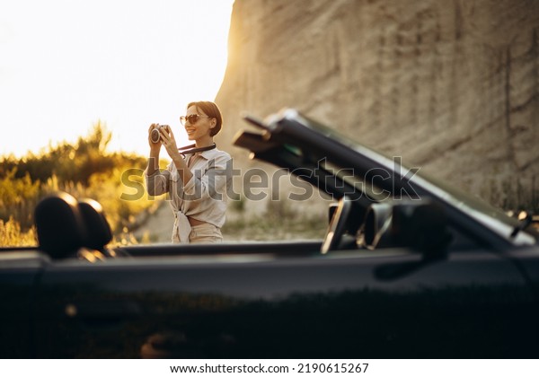 Woman standing by car and making photos of\
mountains on the sunset