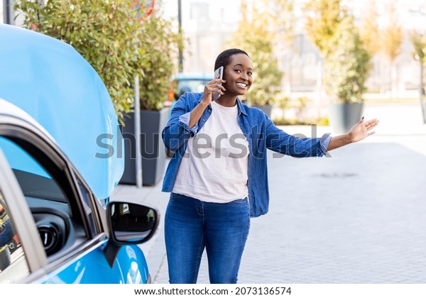 Woman standing by her broken car on the road and\
using phone to call for help. Calling Emergency Service. Cheerful\
young woman with car troubles calling for roadside assistance -\
Insurance concepts