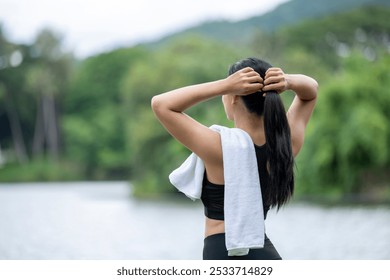 A woman is standing by a lake with her hair in a ponytail and a towel draped over her shoulder - Powered by Shutterstock