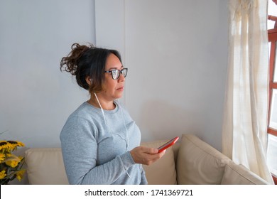 woman standing by the window talking on her cell phone after waking up in the morning