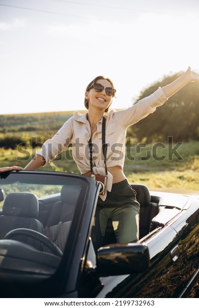Woman\
standing in car cabriolet with camera on her\
neck