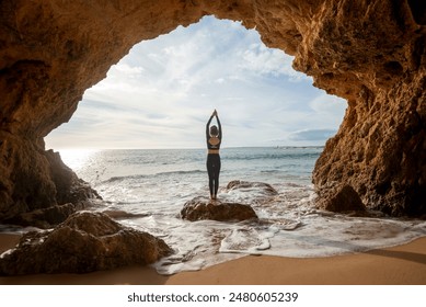 Woman standing in a cave by the sea, meditating and practicing yoga - Powered by Shutterstock