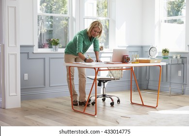 Woman Standing At Desk Working At Laptop In Home Office