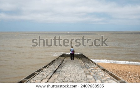 Woman standing at the edge of a Slipway in the ocean. Cloudy sky. Whitstable kent