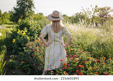 Woman standing in flower garden. Female florist relaxing and enjoying view at blooming floral farm in summer