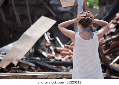 woman standing in front of burned out house and holding her head with both hands