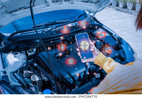 A woman standing in front of a\
car with a bonnet Overlooking the engine room And is using the\
phone to contact the auto repair center Via smartphone\
app