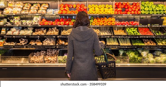 Woman standing in front of a row of produce in a grocery store. 