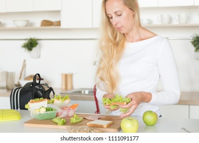 Woman Is Standing In Her Kitchen,holding Sandwich.Mom Preparing School Snack Or Lunch For Her Child In Home Kitchen.Homemade School Sandwiches.Packing In School Lunchbox.Lunch Box With Appetizing Food