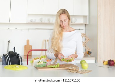 Woman Is Standing In Her Kitchen,holding Sandwich.Mom Preparing School Snack Or Lunch For Her Child In Home Kitchen.Homemade School Sandwiches.Packing In School Lunchbox.Lunch Box With Appetizing Food