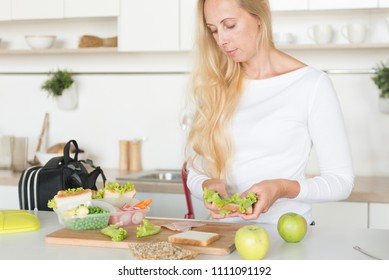 Woman Is Standing In Her Kitchen,holding Sandwich.Mom Preparing School Snack Or Lunch For Her Child In Home Kitchen.Homemade School Sandwiches.Packing In School Lunchbox.Lunch Box With Appetizing Food