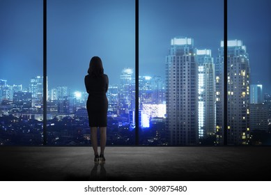 Woman Standing In His Office Looking At The City At Night. Business Success Concept