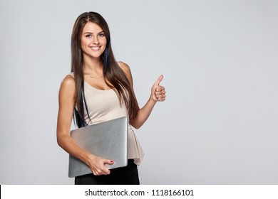 Woman Standing Holding Closed Laptop, Looking At Camera Smiling And Gesturing Thumb Up