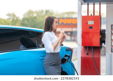 Woman standing holding a cup of coffee while waiting to charge an electric car at a city public charger station