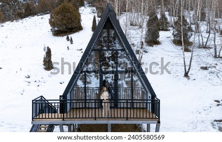 Woman standing and holding cup of tea on the balcony of A Frame cabin in the winter park